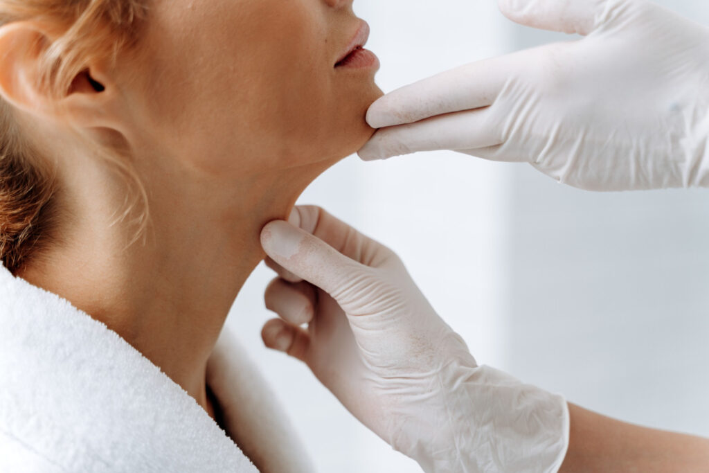 A provider at Chandler Eye Care, wearing surgical gloves, examines a patient's neck and jawline. The provider is ensuring that a non-surgical necklift near Short Pump would align with this patient's specific needs. 