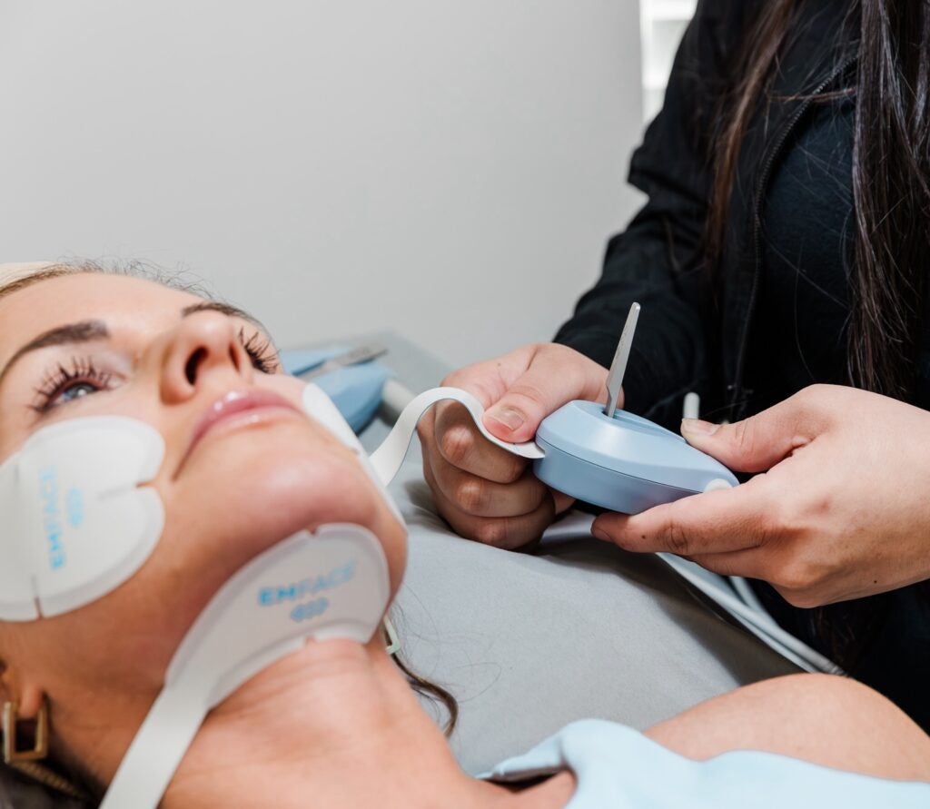 A provider at Chandler Eye Care adjusts the settings on a patient's non-surgical necklift near Short Pump using Emface. The special Emface applicators use both HIFES and RF energy to improve the appearance of the chin and jawline, which the provider can adjust to meet the patient's needs. 